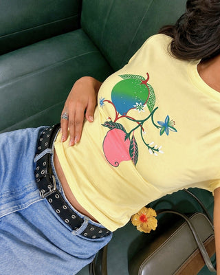 Model wearing a butter-yellow T-shirt with a colorful mango graphic, paired with blue jeans and a black belt