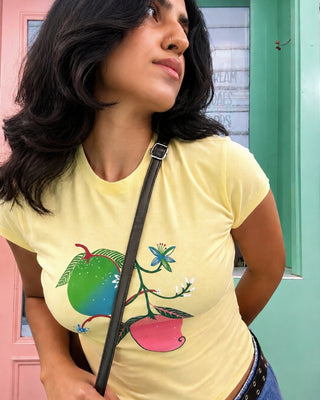 Close-up of colorful hand-drawn mango graphic on butter yellow tee at a cafe
