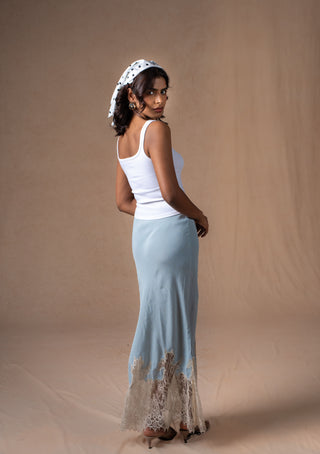 A woman wearing a white gelato ribbed tank top and a light blue maxi skirt with a lace hem