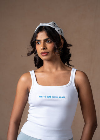 Model wearing a white scoop-neck Gelato tank top with the text 'PRETTY SURE I NEED GELATO' printed in blue on the chest