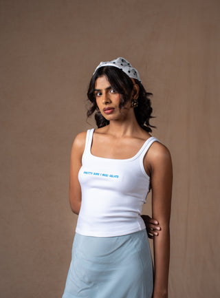 A model wearing a white ribbed tank top with blue embroidered 'pretty sure i need a gelato' text on the chest paired with a blue lace skirt