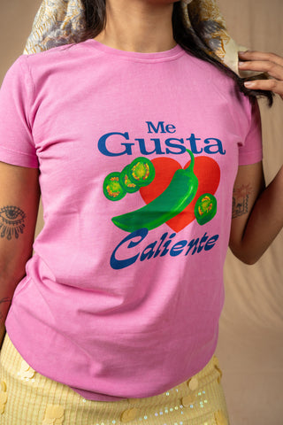A close-up of a model wearing a pink sweet & spicy graphic T-shirt with the Spanish text 'Me Gusta Caliente' and a colorful chili pepper and hot illustration on the front.